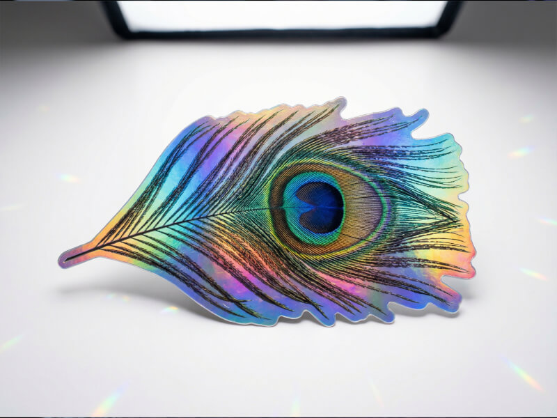 Stansad hologramklistermärke med detaljerat tryck och regnbågsprisma-reflektioner mot ljus bakgrund