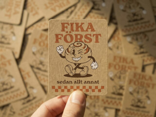 Klistermärke i kraftpapper med retro fika-motiv och kanelbullekaraktär på vit bakgrund