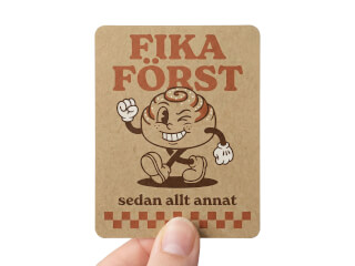 Klistermärke i kraftpapper med retro fika-motiv och kanelbullekaraktär på vit bakgrund