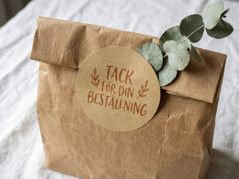 Rund kraftpappersdekal med texten tack för din beställning på brun förpackningspåse med eukalyptus