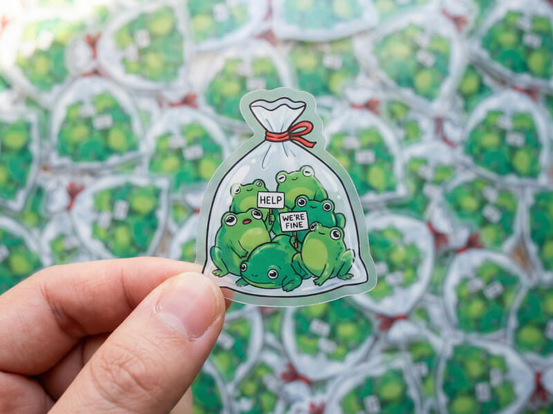 Transparent klistermärke i hand framför stor upplaga med samma motiv