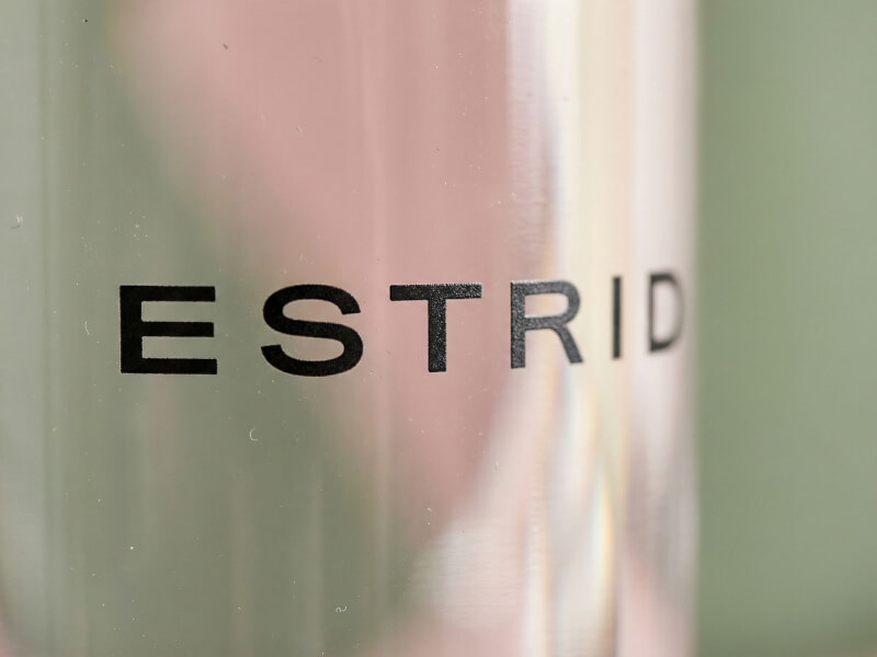 Närbild med mjukt fokus på den svarta horisontella logotypen för Estrid på en frostat transparent flaska