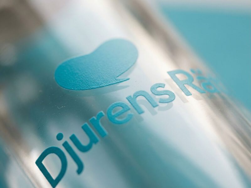 Närbild på en turkos Djurens Rätt-logotyp tryckt på en transparent vattenflaska i färgstarkt dagsljus