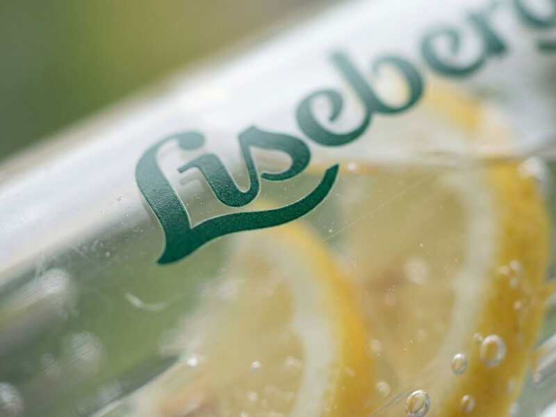 Makro-närbild av grön Liseberg-logotyp tryckt på en transparent vattenflaska fylld med skivad citron