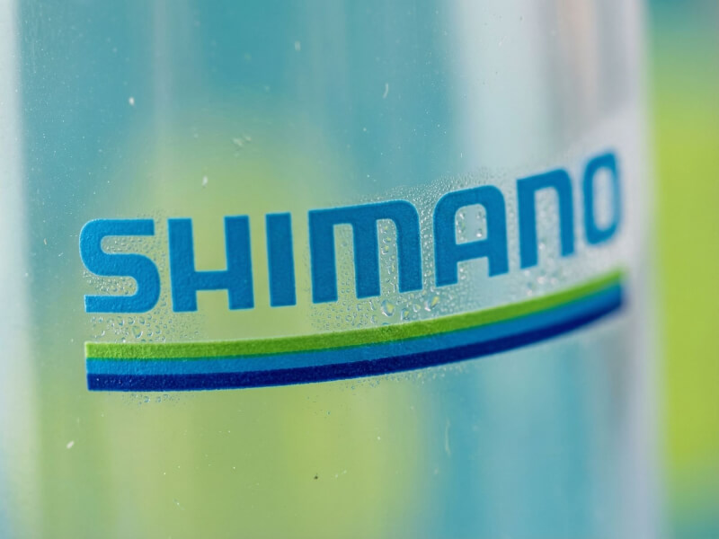 Närbild på den välbekanta blå Shimano-logotypen tryckt över en grön och marinblå linje på en kondensfylld sportflaska