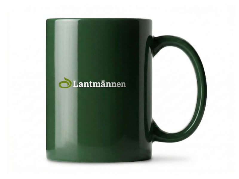 Mörkgrön blank kaffemugg Santos med tryckt Lantmännen-logotyp mot vit bakgrund.