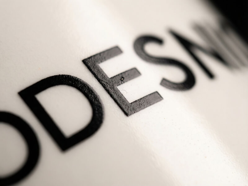 Närbild på en vit kaffemugg av modellen Bahia med tydligt svart tryck av hög kvalitet, där texturen i texten framhävs mot den matta ytan.