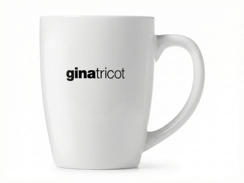 Vit blank kaffemugg Bogota med tryckt svart Gina Tricot-logotyp, isolerad mot vit bakgrund.