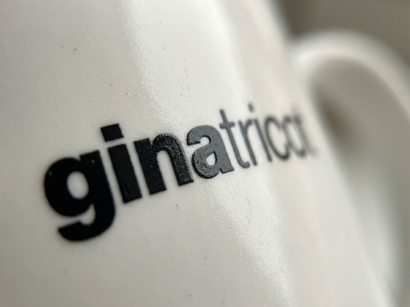 Närbild på en vit, blank keramisk kaffemugg av modellen Bogota med svart tryckt Gina Tricot-logotyp.