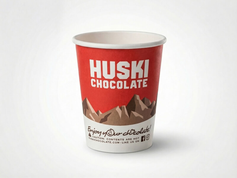 Pappersmugg 22 cl Express med matt röd yta, Huski Chocolate-logotyp och tryckta bergsmotiv, isolerad mot vit bakgrund.