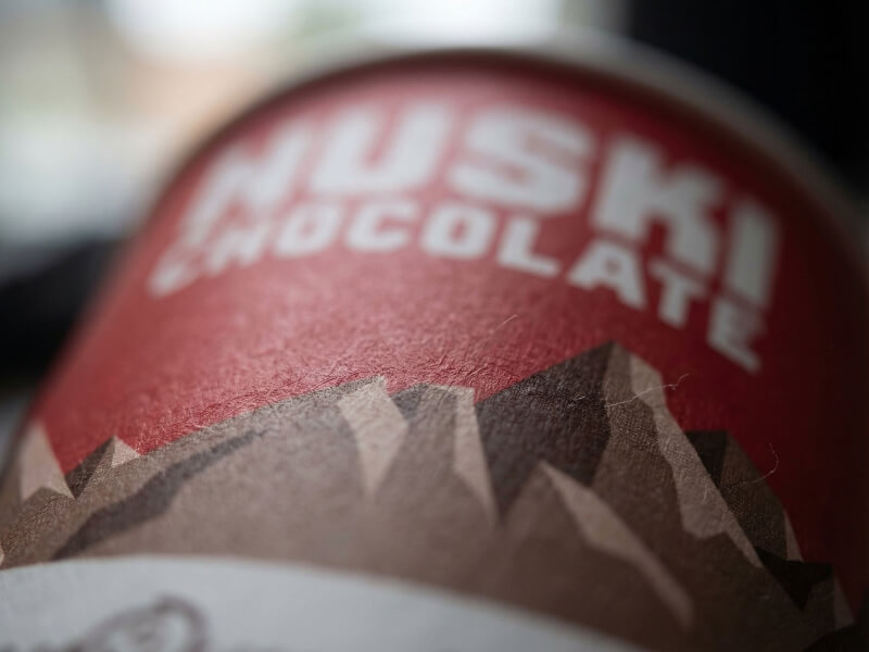 Närbild på en röd pappersmugg 22 cl Express med tryckt logotyp och bergs-grafik i matt finish.