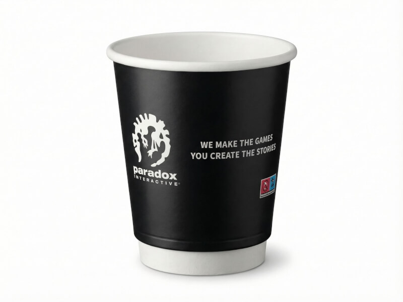 Svart dubbelväggig pappersmugg på 24 cl med Paradox Interactive-logotyp och tryckt text, isolerad mot vit bakgrund.