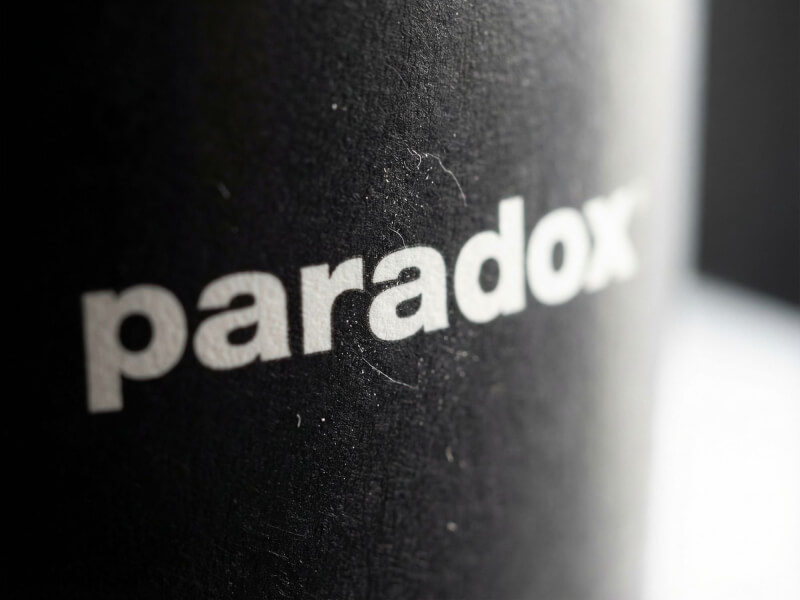 Närbild på en matt svart dubbelväggig pappersmugg med 24 cl volym, prydd med en vit tryckt logotyp för Paradox.