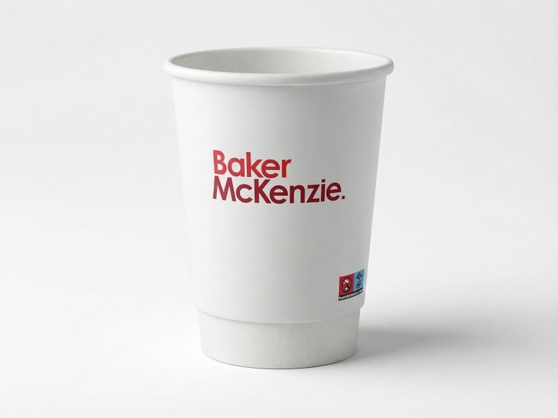 Vit dubbelväggig pappersmugg på 36 cl med röd logotyp för Baker McKenzie, fotograferad mot en neutral studiobakgrund.