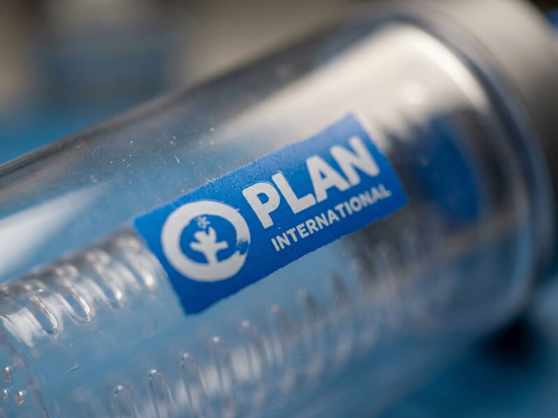 Närbild på blå Plan International-logotyp tryckt på en vattenflaska med invändig infuser-kammare
