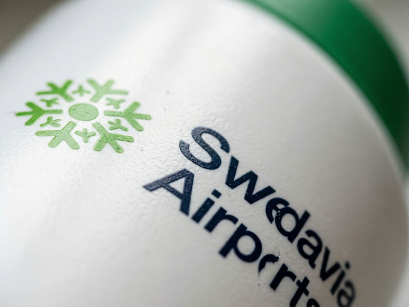 Närbild på den gröna och blåa logotypen för Swedavia Airports tryckt på en vit sportflaska