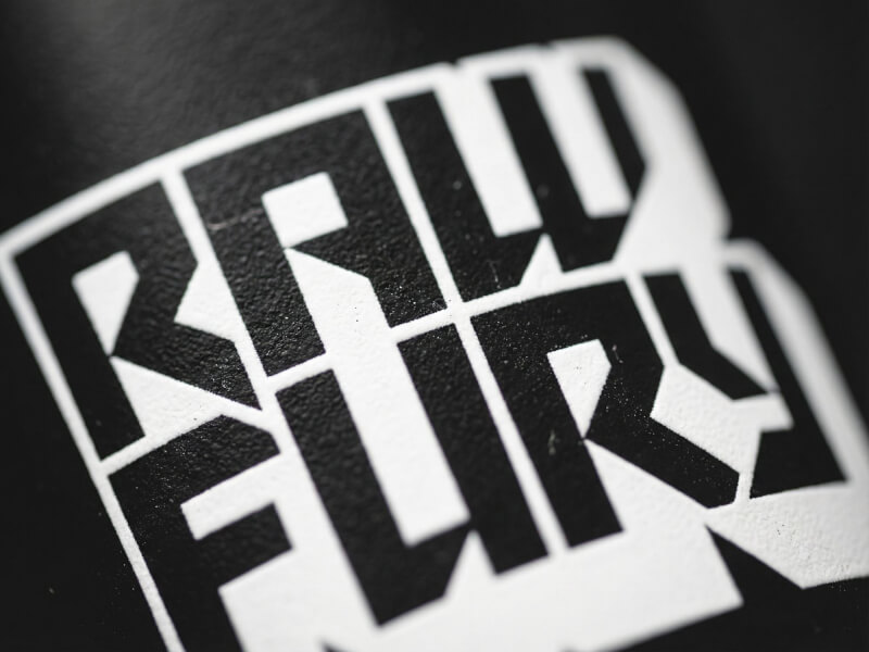 Närbildsdynamisk vinkel av en vit fet Raw Fury-logotyp tryckt på en svart sportflaska