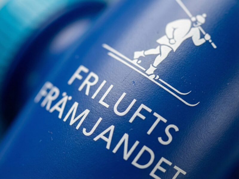 Detaljrik närbild av en vit illustration med skidåkare samt texten Friluftsfrämjandet tryckt på en texturerad blå sportflaska