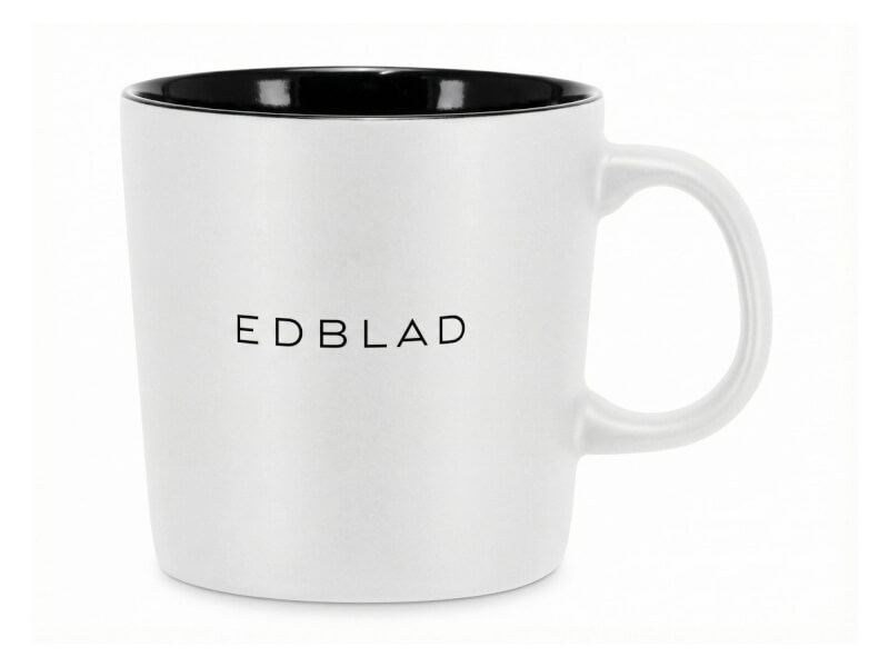 Stengodsmugg Emma Vit med svart insida och Edblad-logotyp tryckt på utsidan mot en vit bakgrund.