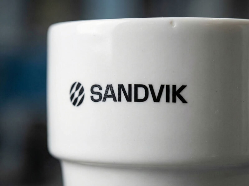 Närbild på en vit, blank porslinsmugg av modellen Stella med Sandviks logotyp tryckt i svart.