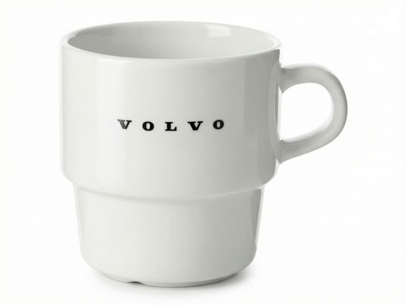 Vit blank porslinsmugg modell Stina med tryckt svart Volvo-logotyp, isolerad mot vit bakgrund.