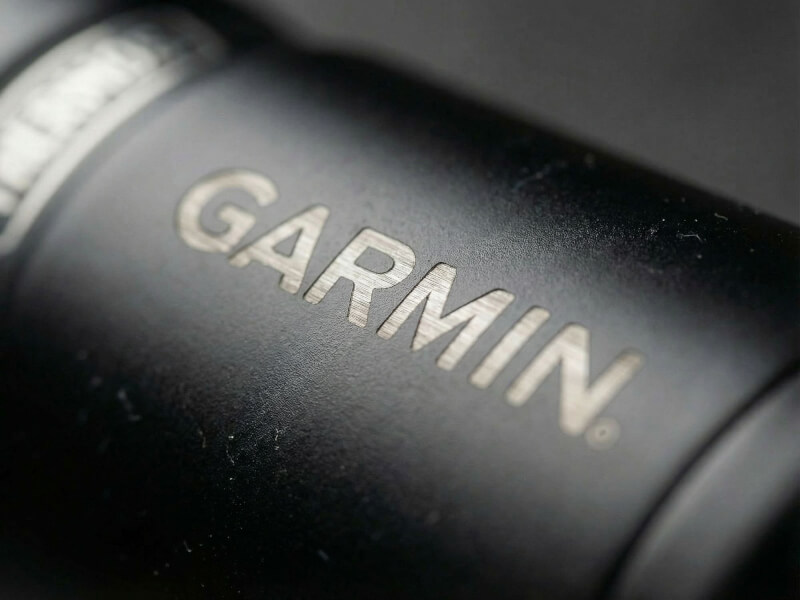 Dramatisk vinklad närbild av silverskarp, ruffig lasergravyr av Garmins logotyp på en texturerad mörk termos