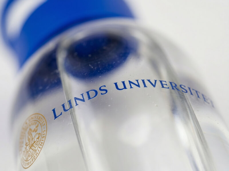 Närbild med kort skärpedjup av logotypen för Lunds Universitet tryckt på en transparent Tritan-vattenflaska