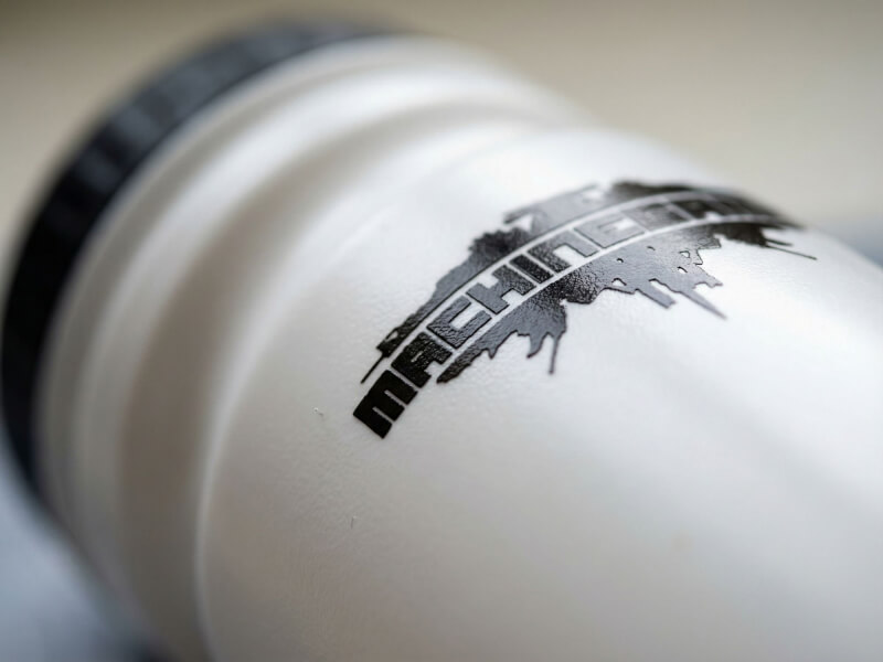 Närbild av den distinkta svarta MachineGames-logotypen tryckt på en greppvänlig vit sportflaska