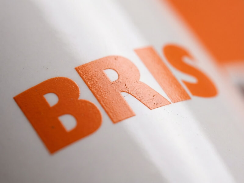 Närbild på en vit stengodsmugg Emma med orange tryckt logotyp av BRIS, som visar den högblanka ytan och tryckkvaliteten.