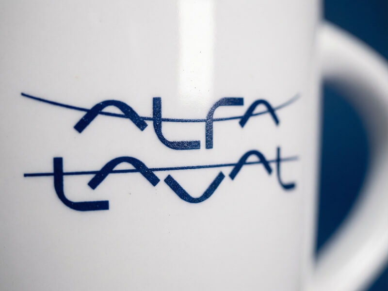 Närbild på en vit, glansig kaffemugg av modellen Aztec med en mörkblå logotyp tryckt med tampotryck.