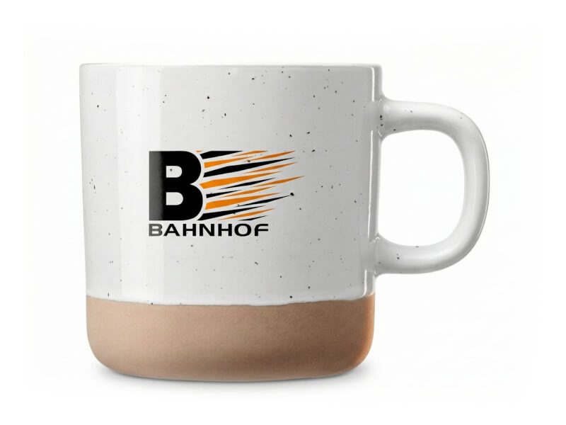 Kaffemugg Pascal i keramik med vit, stänkmönstrad glaserad ovandel och beige matt bas, profilerad med Bahnhofs logotyp tryckt på framsidan.