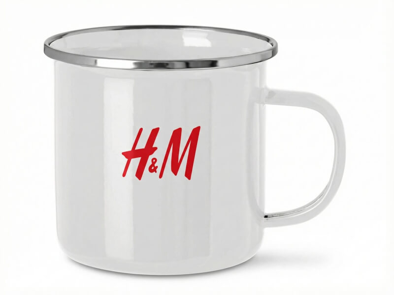 Vit Kaffemugg Camp i emaljerad stil med blank finish och silverfärgad kant, prydd med röd H&M-logotyp.