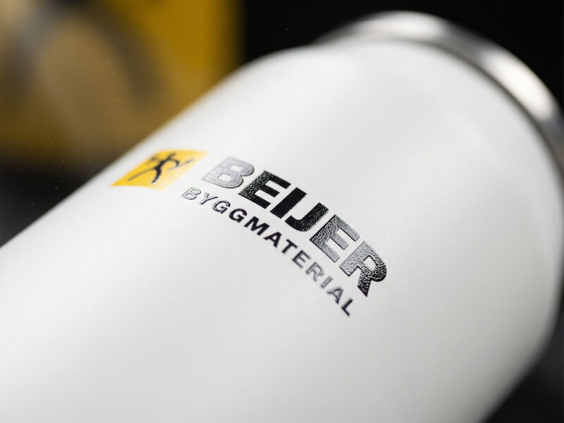 Närbild på en vit termosmugg Can 280 med en blankt upphöjd UV-tryckt logotyp för Beijer Byggmaterial.
