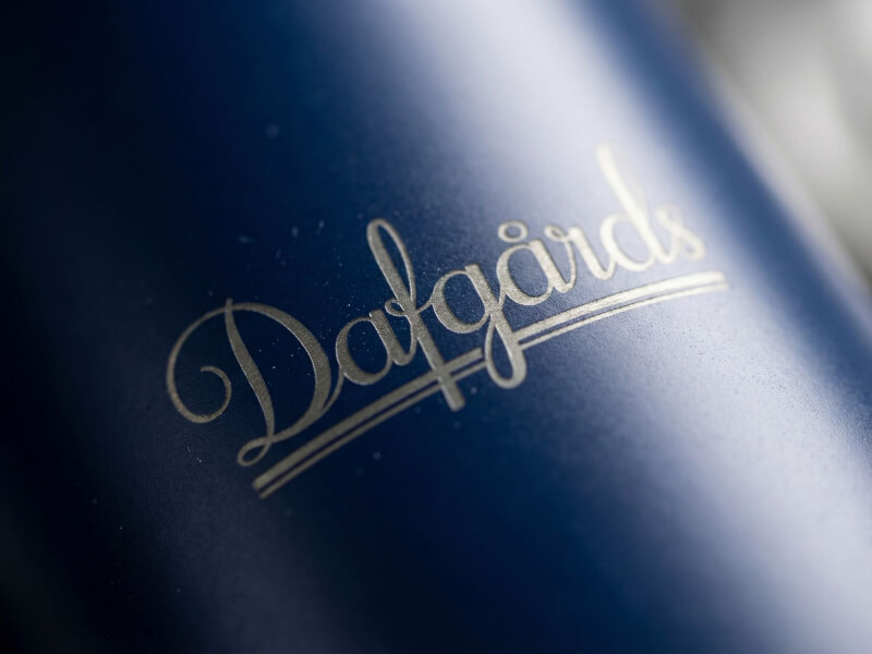Mörkblå mattsvart yta varpå Dafgårds eleganta skrivstilslogotyp är vackert ingraverad, reflekterande ett brons/guldaktigt stållager