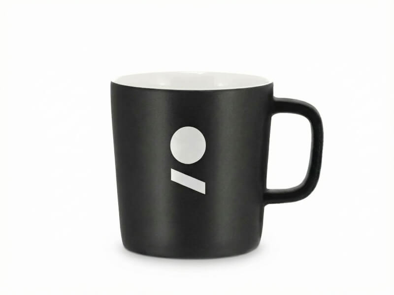 Stengodsmugg Ebba Svart med matt finish och vit insida, dekorerad med ett vitt tryckt logotypsymbol mot vit bakgrund.