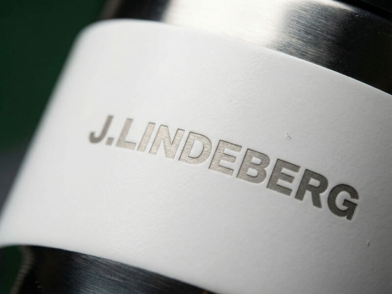 Närbild på en vit termosmugg Contour med J.Lindeberg-logotypen applicerad via lasergravyr på en matt, vit yta och detaljer i borstat rostfritt stål.