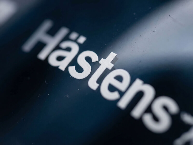Närbild i skarpt solljus på vit vertikal Hästens-logotyp tryckt på en mörktonad vattenflaska