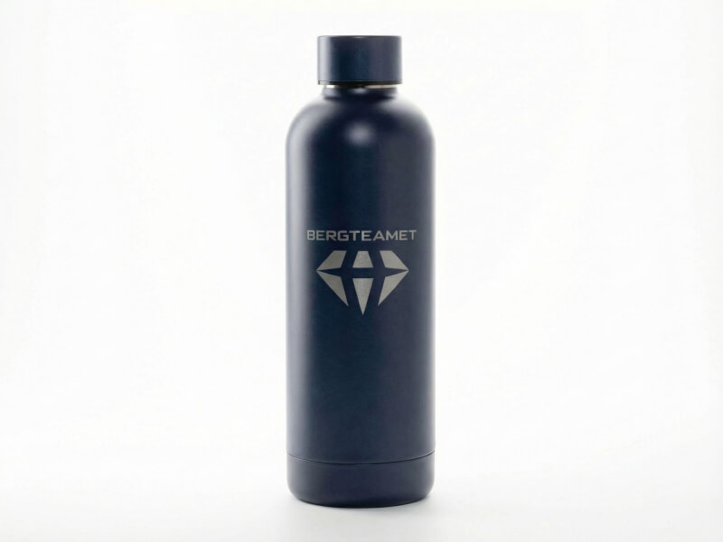 Mörkblå slät termosflaska med metalliskt lock och elegant silverfärgad lasergravyr för Bergteamet centralt placerad på vit bakgrund