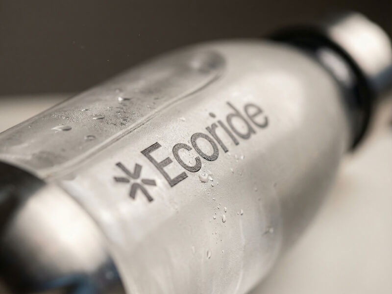 Närbild på kondens och Ecoride-logotyp tryckt på en transparent glasvattenflaska