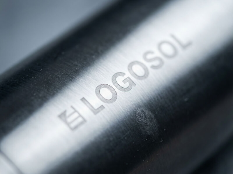 Närbild med mjuk oskärpa av den blänkande lasergraveringen Logosol vertikalt placerad över en borstad metallisk termosyta