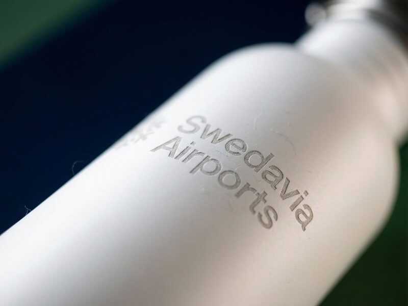 Närbild på en elegant och diskret silvergraverad Swedavia Airports-logotyp på en vit stålvattenflaska