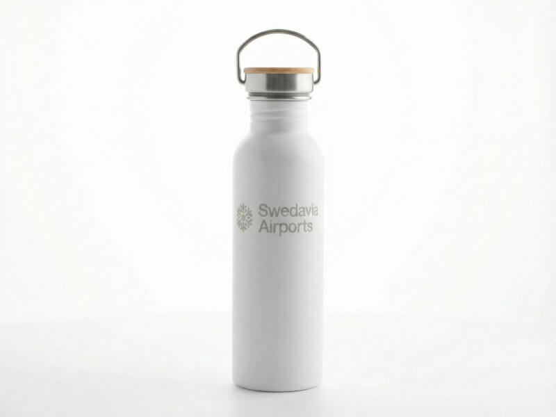 Vit stålvattenflaska med silverfärgat lock och bygel, ljust graverad Swedavia Airports-logotyp på vit bakgrund
