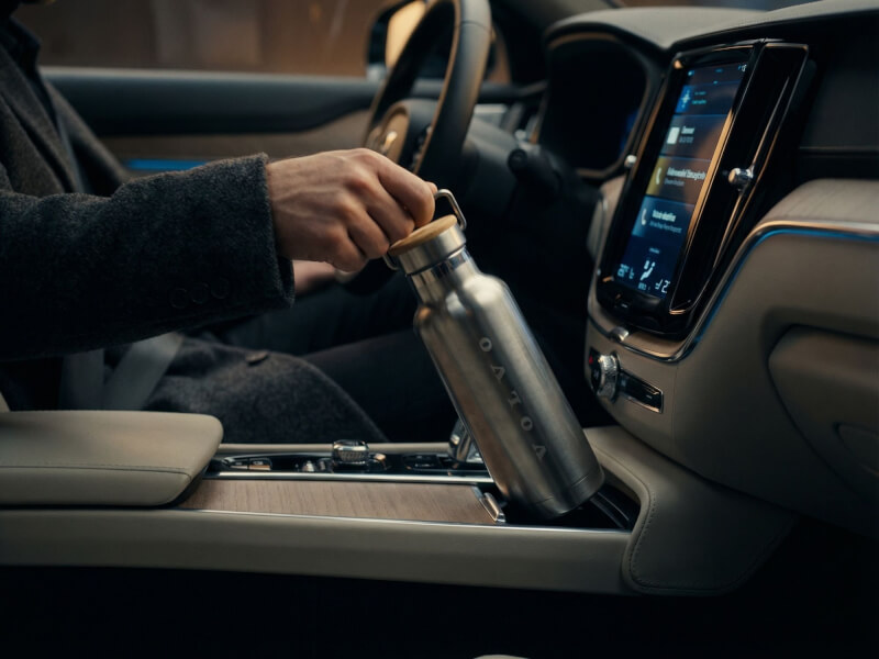 En hand som håller en rostfri Termosflaska Thor 480 med bambulock och lasergraverad logotyp i en bils mugghållare.