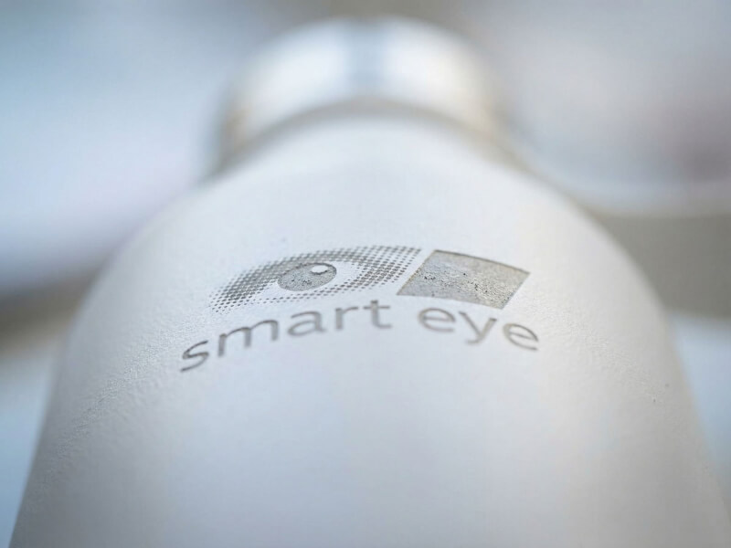 Ett krispigt detaljfoto av Smart Eyes logotyp exakt lasergraverad in på termosens matta, stenvita ytskikt