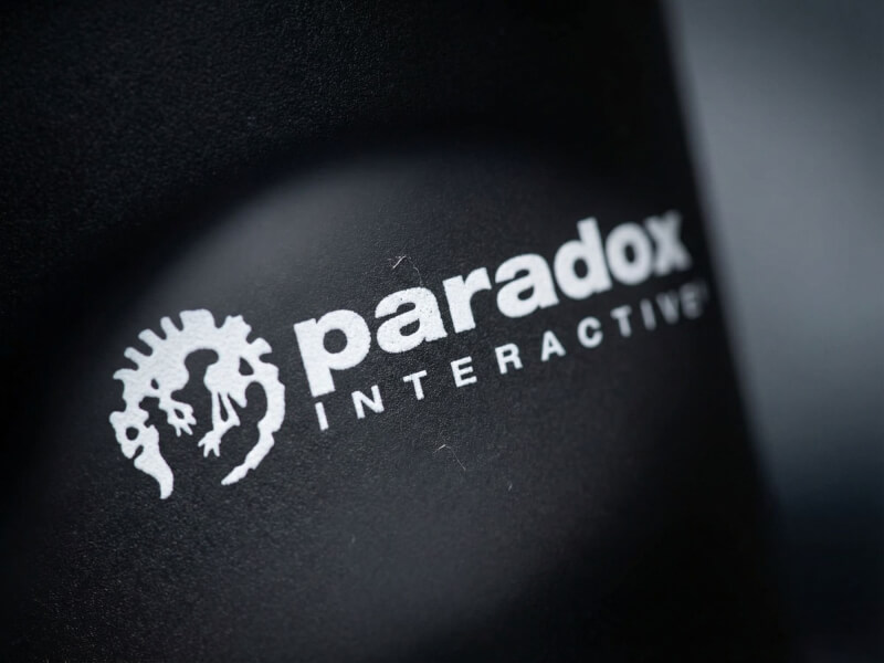 Närbild på en matt svart Plastmugg Americano med Paradox Interactive-logotypen tryckt i vitt, lämplig som profilprodukt för kontoret.