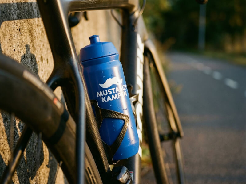 Blå Mustaschkampen sportflaska säkert placerad i flaskstället på en tävlingscykel parkerad vid en naturskön väg