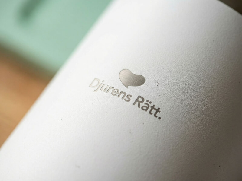 Närbild på en vit termosmugg av modellen Sydney med Djurens Rätts logotyp fint laserograverad i den matta ytan.