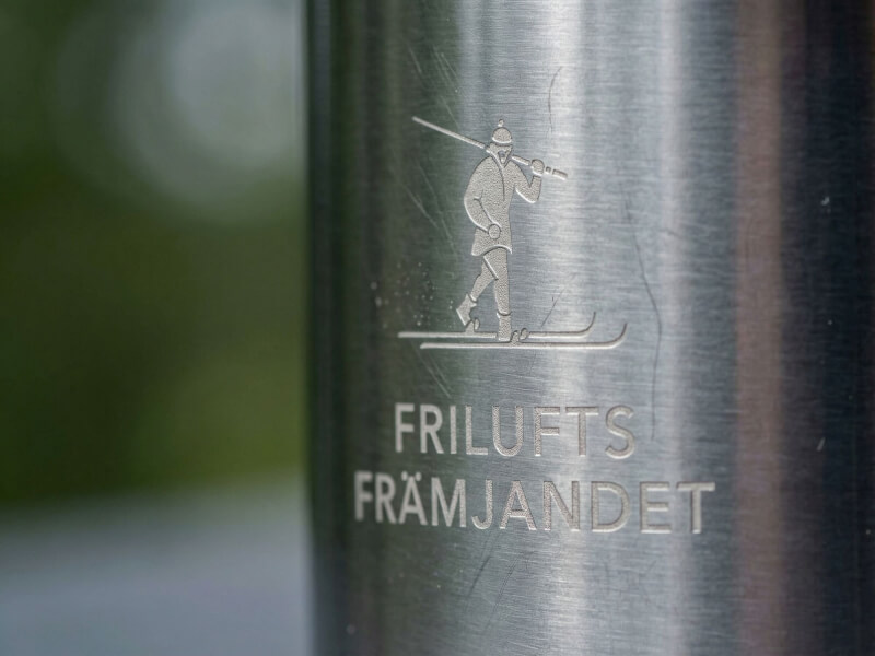 Närbild på en kaffemugg Nunavut i rostfritt stål med en stilren laserngraverad logotyp för Friluftsfrämjandet utomhus i naturlig miljö.