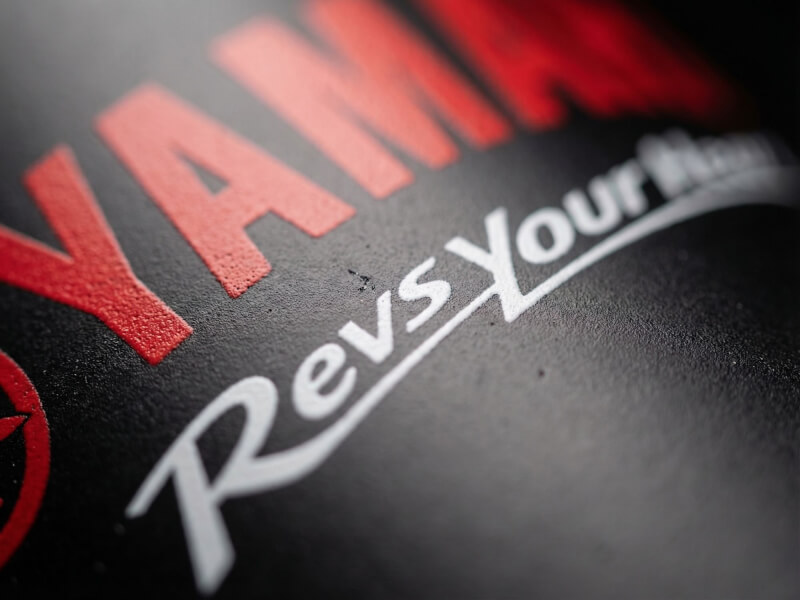 Närbild på en texturerad svart yta av en stålvattenflaska med Yamaha-logotyp tryckt i rött och vitt